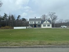 a large white house sitting on the side of a road next to a lush green field