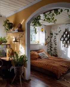 a bed sitting under a window next to a wooden table and chair with potted plants on it