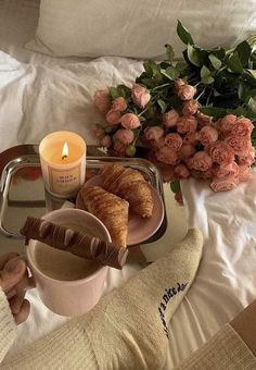 a tray with croissants, coffee and flowers on top of a bed