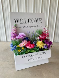 a welcome sign sitting on top of a white box filled with lots of colorful flowers