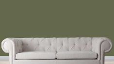 a white couch sitting on top of a hard wood floor next to a green wall