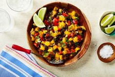 a wooden bowl filled with pineapple salsa next to two bowls of salt and limes