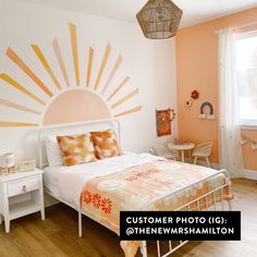 a bed room with a neatly made bed and a sun painted on the wall above it