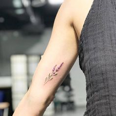 a woman's arm with a small purple flower tattoo on the left side of her arm