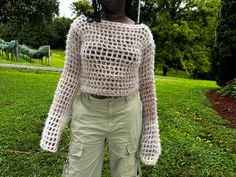 a woman standing in the grass with an umbrella over her head and wearing green pants