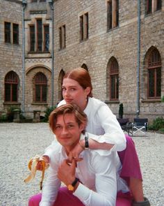 two people sitting on the ground in front of a building