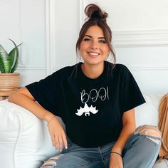 a woman sitting on a couch wearing a black t - shirt with the word boo printed on it