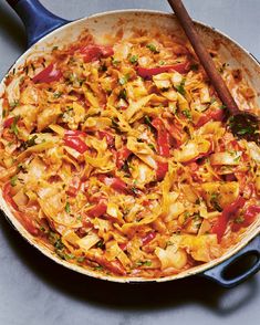 a skillet filled with pasta and vegetables on top of a counter next to a wooden spoon