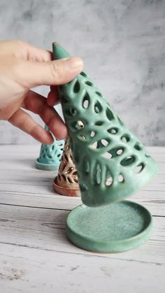 a hand holding a green ceramic object on top of a white wooden table next to other items