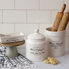 two white canisters sitting on top of a counter next to cookies and utensils