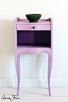 a small purple table with a green bowl on it's top, against a white wall