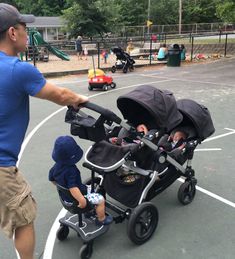 a man pushing a stroller next to a small child in a blue shirt and tan shorts