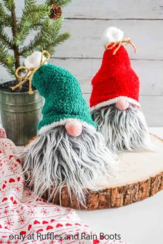 two knitted gnomes sitting on top of a wooden slice next to a christmas tree