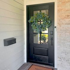 a black front door with a wreath on it and a welcome mat in front of it