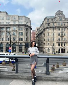 a woman is standing on a bridge in front of some buildings and looking at the camera