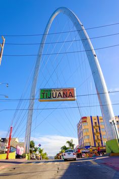 an arch with the word tijuana on it and cars parked under it in front of some buildings