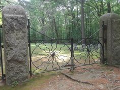 an iron gate in the middle of a wooded area with two large rocks behind it