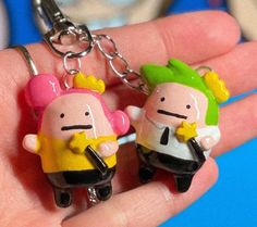 two toy figures are sitting in the palm of a person's hand, one is holding a keychain