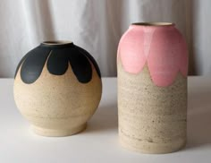 two vases sitting side by side on a white tableclothed surface, one with black and pink glaze