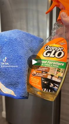 a person is holding a bottle of orange glo cleaner and a blue towel on top of a metal trash can