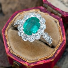 an emerald and diamond ring in a wooden box