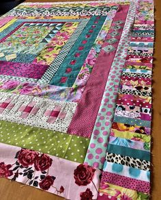 a colorful quilt is laying on top of a wooden table with polka dots and flowers