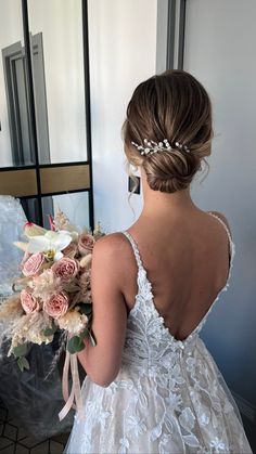 the back of a bride's dress holding a bouquet of flowers in her hand