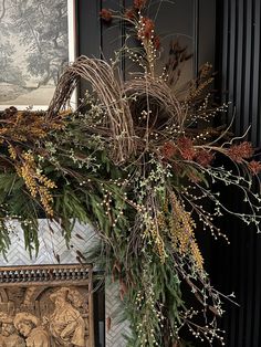 the wreath is hanging on the mantle by the fire place with pine cones and berries