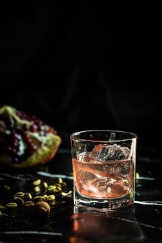 a glass filled with liquid sitting next to a pomegranate on a table