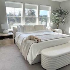 a large white bed sitting in a bedroom next to two windows