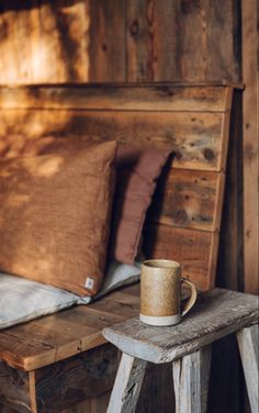 a coffee cup sitting on top of a wooden table next to a bed with pillows