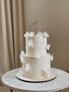 a three tiered white wedding cake with gold leaf decorations and the number six on top