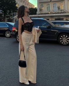 a woman standing in the middle of a parking lot holding a black purse and looking up