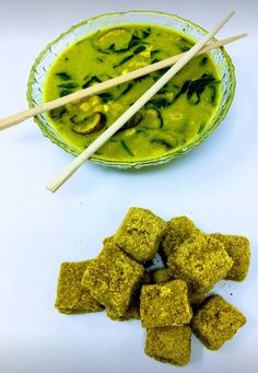 two bowls filled with food next to chopsticks on a white tablecloth and green soup in a bowl