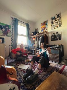 two young boys sitting on the floor playing guitars in a room full of musical instruments