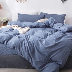 an unmade bed with blue sheets and pillows in a white room next to a lamp