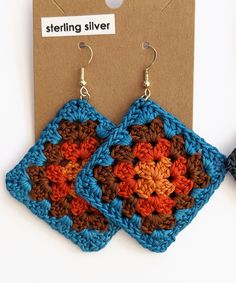 two crocheted square shaped earrings sitting on top of a cardboard box next to each other