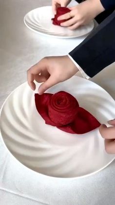 two people are decorating plates with red flowers on them, and one person is holding a piece of cloth