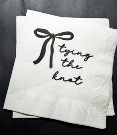 two white napkins with black writing on them and a bow tied around the edges