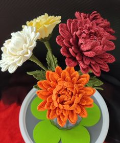 three flowers in a vase on a red and green table cloth with a black background