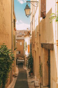 a narrow alley way in an old town with light hanging from the ceiling and potted plants on either side