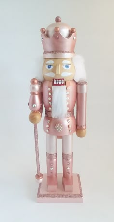 a pink and gold nutcracker is standing on a white surface with a cane