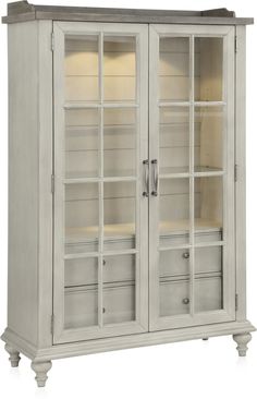 a white cabinet with glass doors on the front and bottom shelves, in an antique style