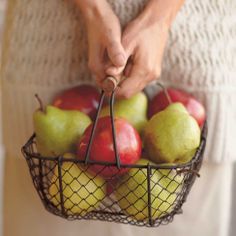 a person is holding a basket full of apples and pears with a wooden stick in it