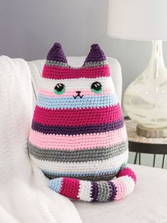 a crocheted cat sitting on top of a white couch next to a lamp