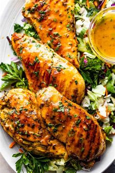 grilled chicken with coleslaw and dressing on a white plate next to a bowl of dipping sauce