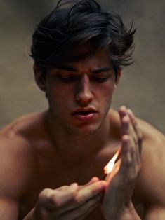 a shirtless man holding a lit candle in his hands while looking at the camera