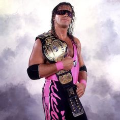 the wrestler is posing for a photo in his pink wrestling outfit and holding two gold belts