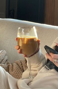 a woman sitting on a couch with a glass of wine and cell phone in her hand