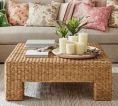 a wicker coffee table with candles and books on it in front of a couch